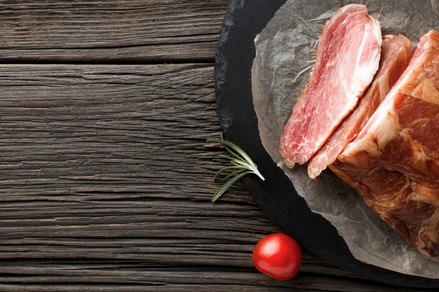 Tranches de porc cru avec romarin sur assiette noire, spécialité Le-raygal-charcuterie dans le Tarn