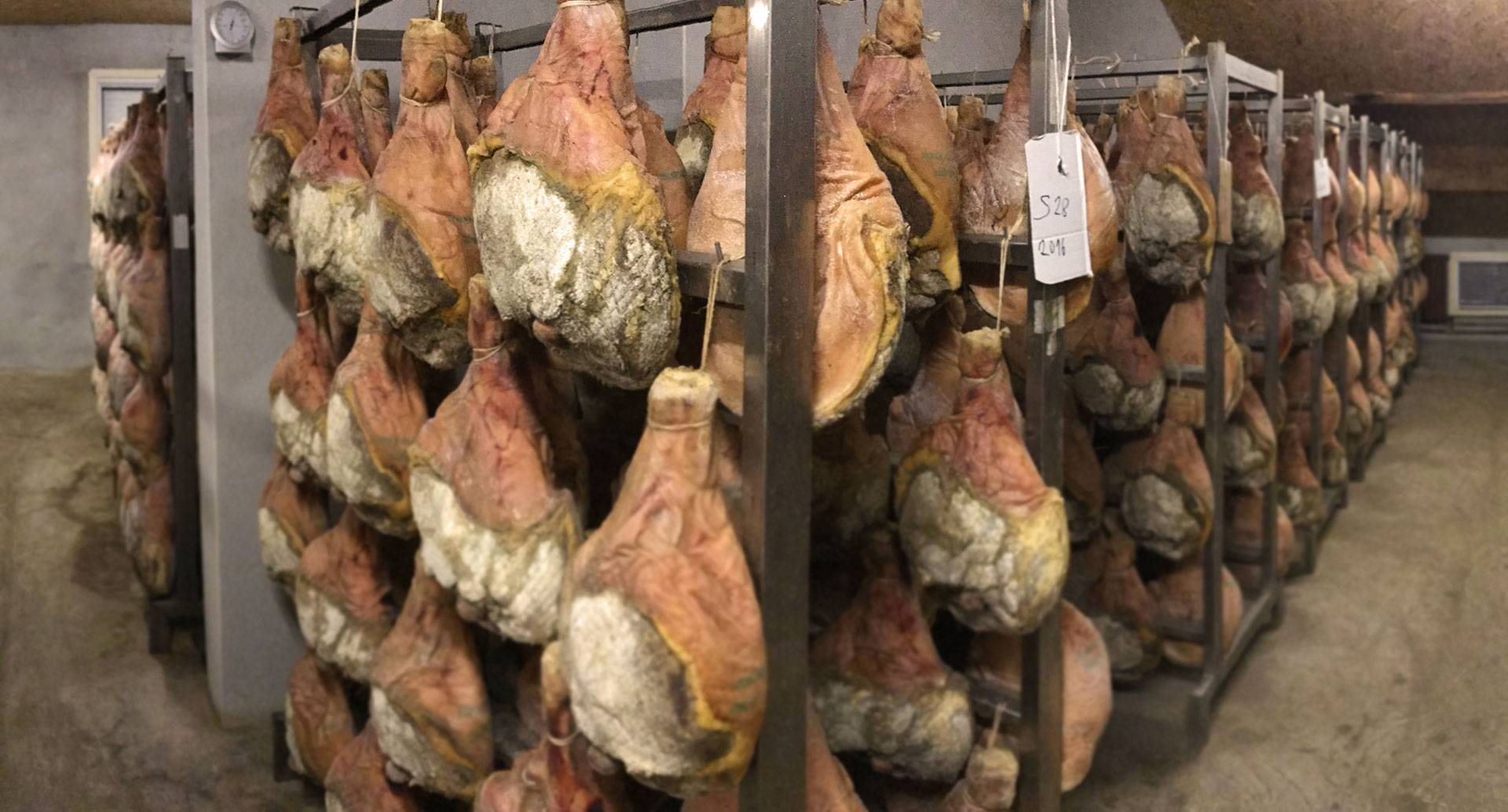 Jambons crus en affinage sur racks métalliques chez Le-raygal-charcuterie, savoir-faire artisanal dans le Tarn